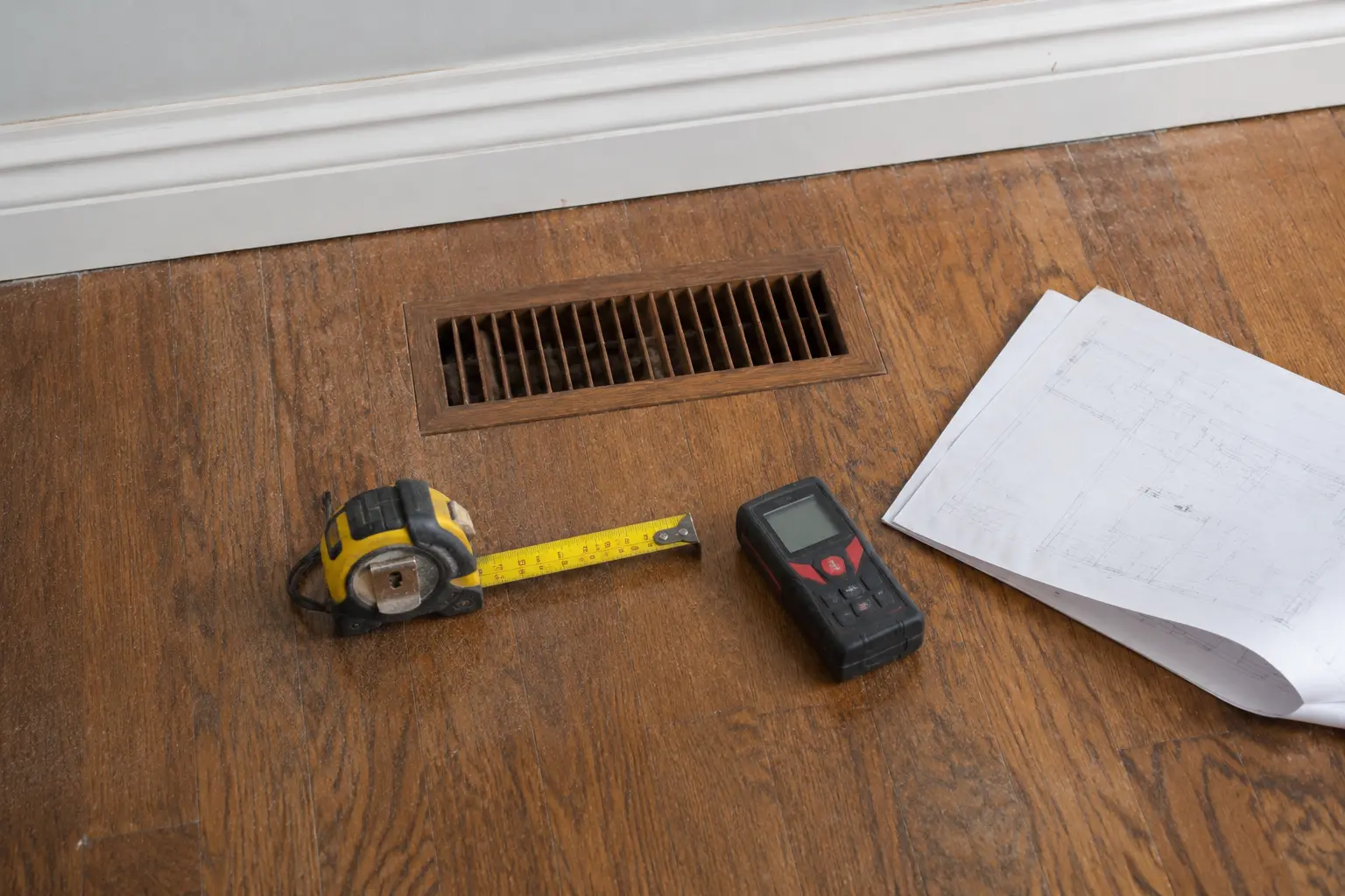 Tape measure and floor plan beside a supply register during a room load survey