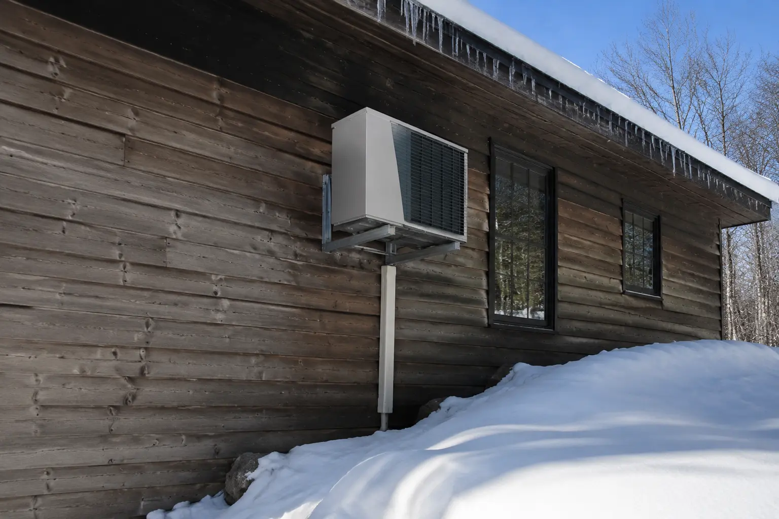 Single-zone heat pump outdoor unit on wall brackets above deep snow